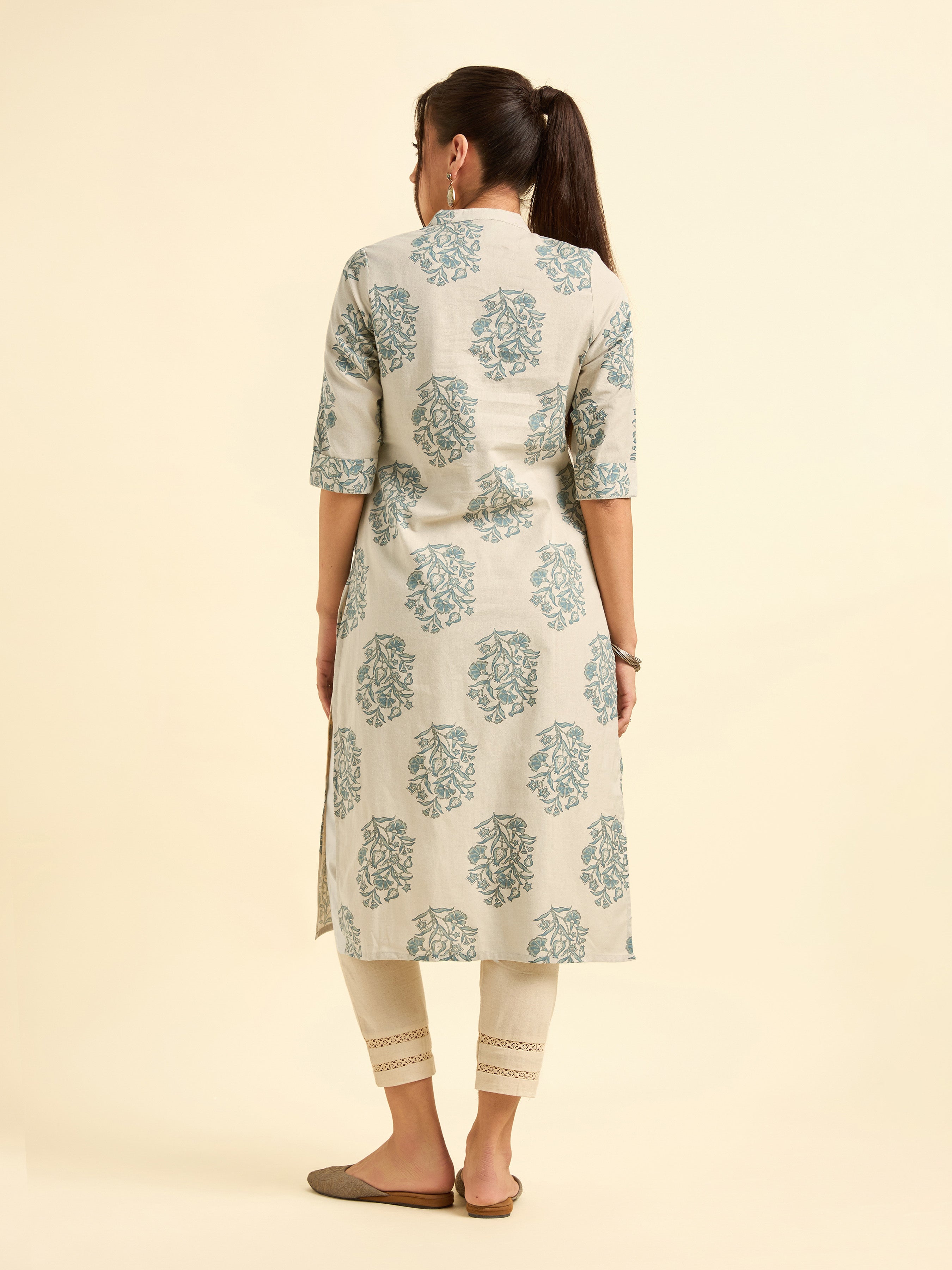 Woman wearing a floral printed kurta with white pants on a beige background